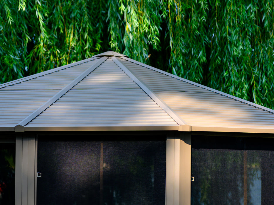Exterior shot of the Gazebo's sand-colored metal roof, highlighting the peak and ridged design against a backdrop of trees.