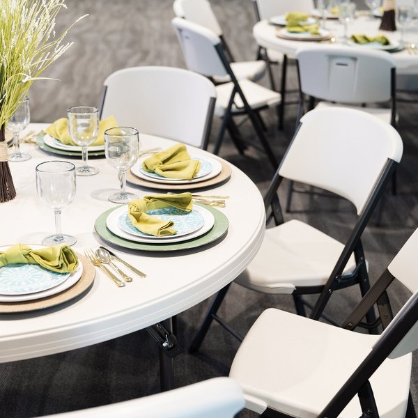 Lifetime round tables and folding chairs set up in a banquet room with full place settings and centerpieces.