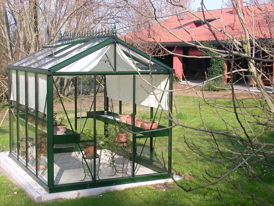 Royal Victorian VI 23 greenhouse with dual shelves, shade cloth panels, and potted plants on a neatly paved base in a spacious backyard setting.