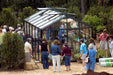 Group of visitors touring the Royal Victorian VI 34 Greenhouse at P. Allen Smith estate, showcasing glass structure and vibrant potted plants.
