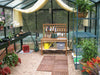 Inside the Royal Victorian VI 34 Greenhouse featuring a wooden potting bench, gardening tools, potted plants, and gravel flooring.
