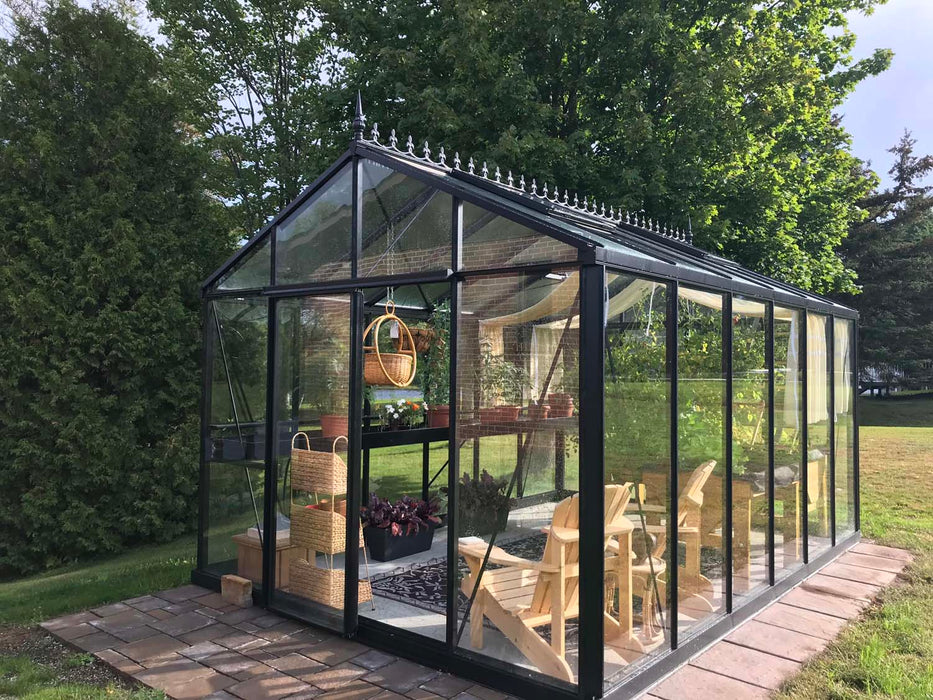 Royal Victorian VI 34 Greenhouse with wooden chairs, hanging basket, and curtain shades, set on a brick walkway surrounded by lush green lawn.