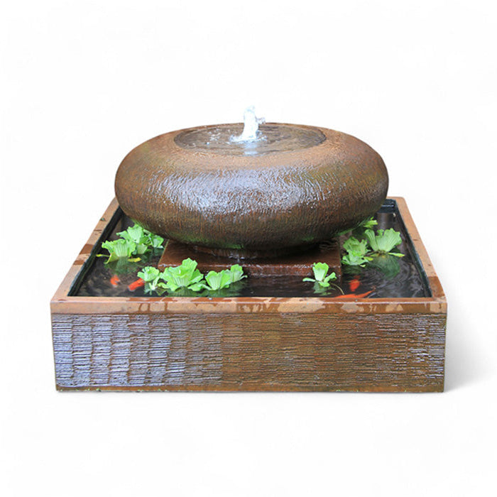 The Exaco Moon Pot Fountain in a rustic brown stone finish, styled as a mini pond with small goldfish and floating green plants in the square water basin.