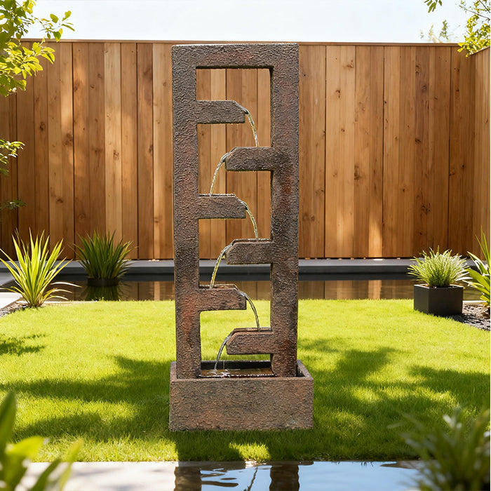 Rustic cascade garden water fountain featuring four tiered spouts, set on green lawn with wood privacy fence backdrop