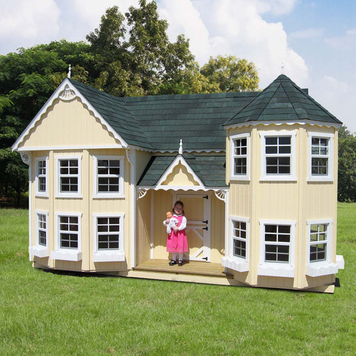 Little Cottage Co. Sara’s Victorian Mansion playhouse in yellow with green roof and turret, child standing at porch holding doll for scale