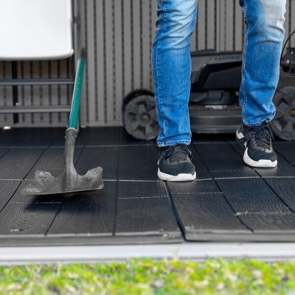 Person installing the Lifetime storage shed's HDPE floor panels with a hand tool, mower visible nearby.
