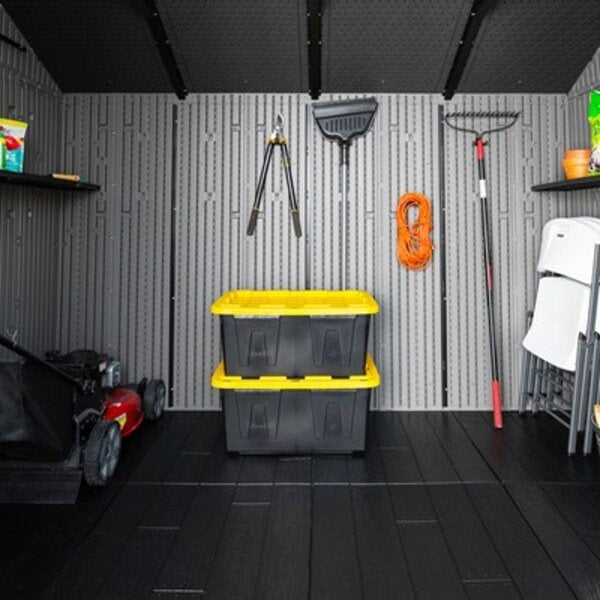 Interior view of the Lifetime storage shed with shelving, a mower, storage bins, and folding chairs.
