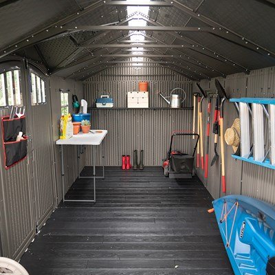 Interior view of the Lifetime 20x8 ft. storage shed showing shelving, a table, tools, and a kayak.