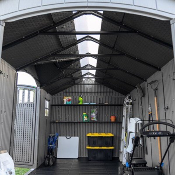 Wide interior view of the Lifetime dual entry storage shed showing skylights, shelving, ladder, and a mower stored inside.