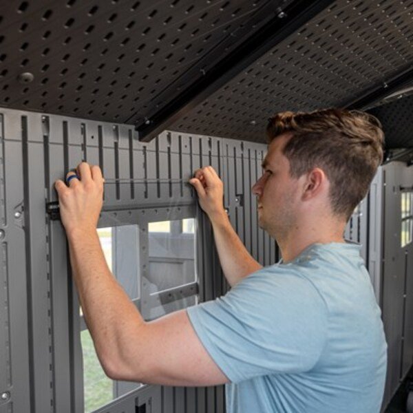 Man installing an interior wall panel inside the Lifetime dual entry storage shed during assembly.