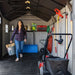 Interior view of the Lifetime dual entry storage shed with a woman carrying a bucket, shelving and mower visible.