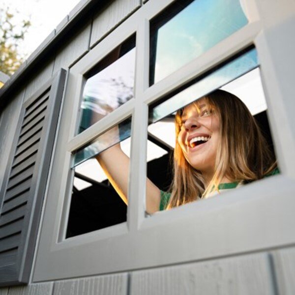 Close-up of a woman opening the Lifetime storage shed's window with decorative shutters.
