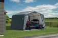 Gray ShelterLogic shed  on a lush green field. This portable shed provides shade and shelter for lawn mowers, tools, and more