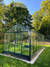Side angle view of Exaco Janssens Royal Victorian VI 36 Greenhouse on a white stone base, showcasing clear glass walls and lush plants inside.