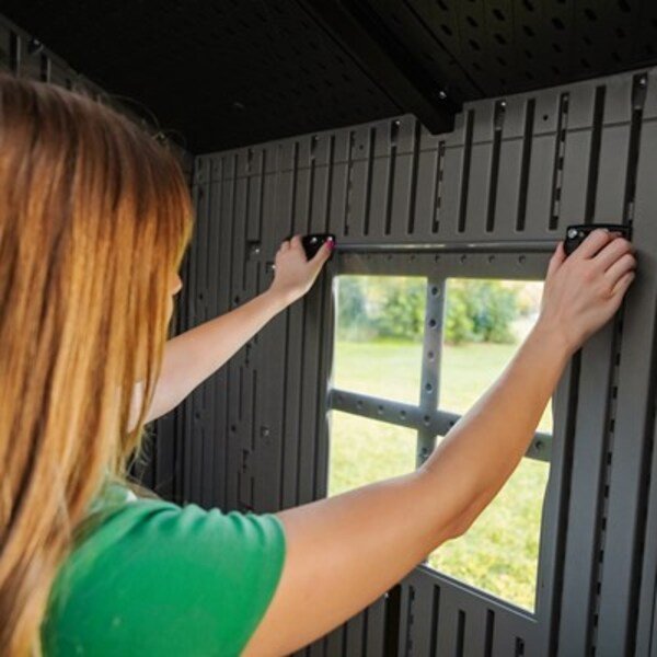 Interior view of a woman installing the Lifetime storage shed's window frame.