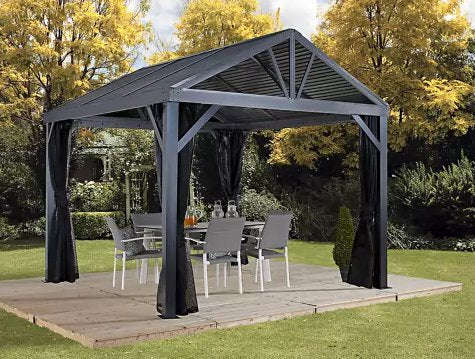 ojag South Beach I Hardtop Gazebo 12x12 ft in Light Gray, set up on a wooden deck in a lush garden, showcasing the spacious and elegant outdoor shelter with dining furniture.