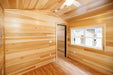 Corner view of the bedroom of Firestack Cabin with natural wood colored walls and flooring with doorway and windows. 