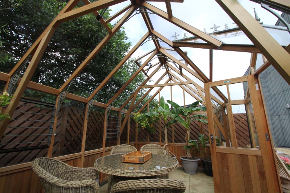 Spacious interior view of the Alton Cambridge Cedar Greenhouse with wicker furniture and lush greenery.