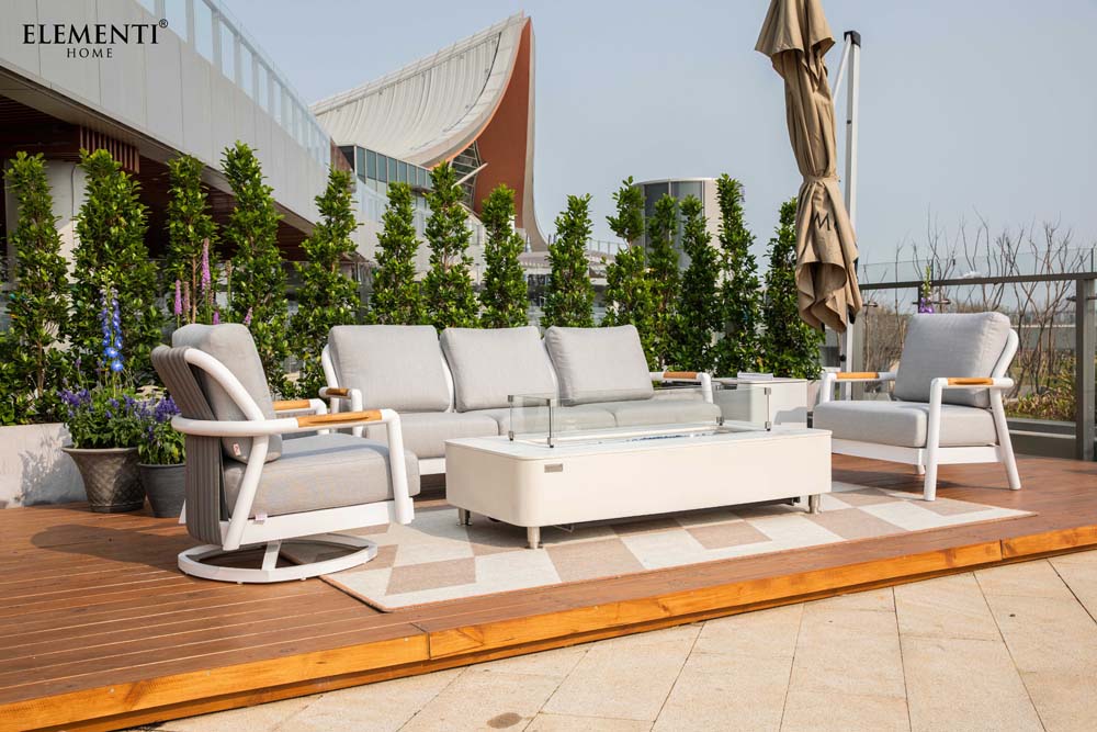 An Elementi Outdoor Furnitures Santorini Collection lounge set, featuring a sofa, two chairs, and a central fire table on a wooden deck.