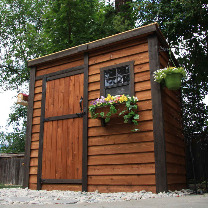 Stained cedar SpaceSaver 8x4 storage shed shown at an angle, featuring a single door and a dark stained wood finish with a hanging flower box.
