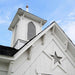 Detailed view of the Star Barn’s steeple cupola showing decorative trim, louvered vents, and copper spire accent above gray roof shingles.