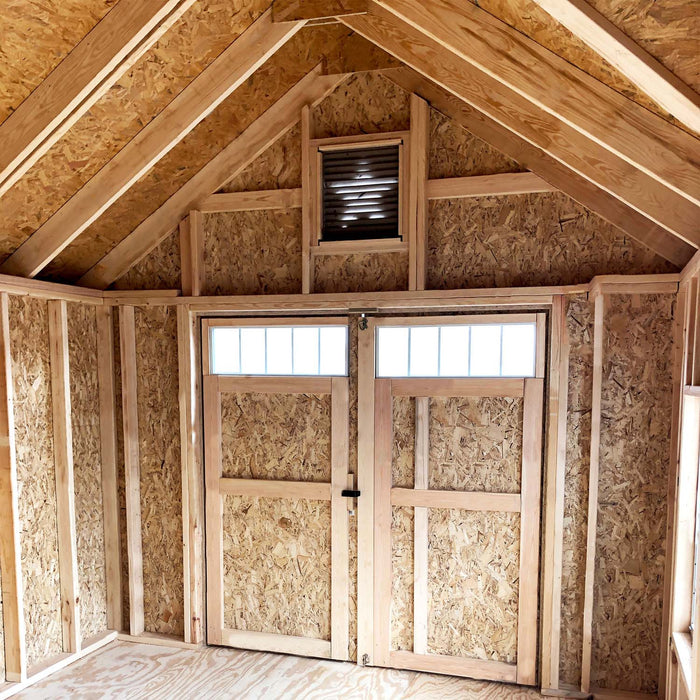 Interior of the Little Cottage Co. Star Barn showing unfinished wooden framing, vent above double doors, and natural plywood flooring.