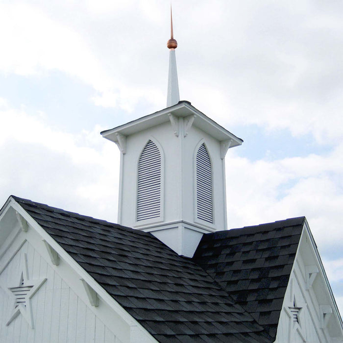 Close-up of Little Cottage Co. Star Barn cupola featuring white arched vents, copper spire tip, and dark shingled roof under blue sky.