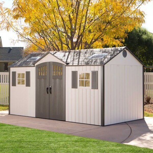Lifetime 15x8 ft. storage shed in a backyard with autumn trees, front angle view with closed doors.