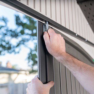 Close-up of a hand installing the Lifetime storage shed's steel door hinge pin.