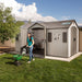 Woman with a lawn spreader next to the Lifetime 15x8 ft. storage shed with open door, mountain backdrop.