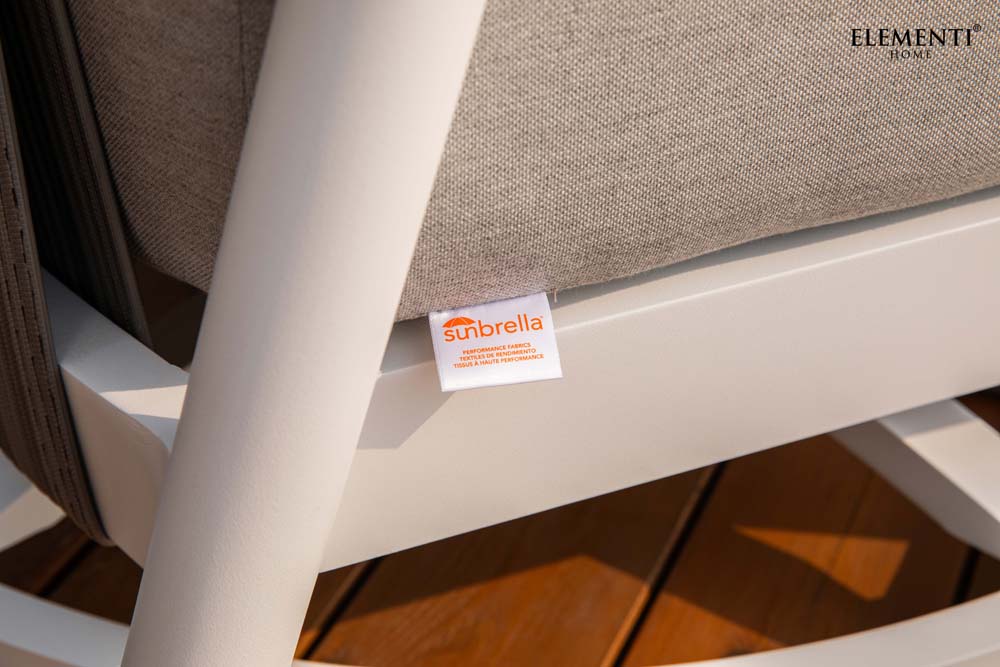 A close-up of a Sunbrella fabric tag on a light brown cushion, part of the Elementi Santorini Collection outdoor furniture.