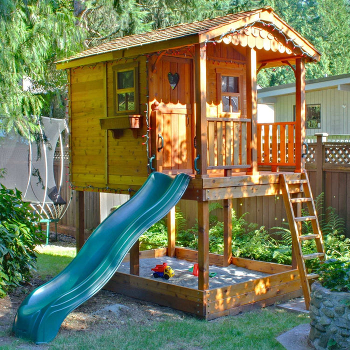 Outdoor Living Today Sunflower Playhouse 6x9 decorated with string lights, featuring a heart cutout door and sandbox with toys