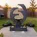 Eclipse outdoor water feature at sunset with illuminated base lights, circular design and cascading water in landscaped backyard patio.