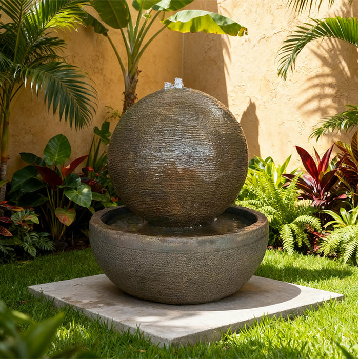 Textured Luna Bowl water fountain featuring a round sphere over basin, placed in a lush tropical garden with vibrant plants.