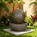 Textured Luna Bowl water fountain featuring a round sphere over basin, placed in a lush tropical garden with vibrant plants.