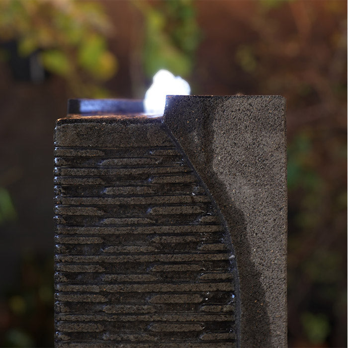 Close up of Yang water fountain corner showing layered stone texture, water flow detail and illuminated top feature at night.