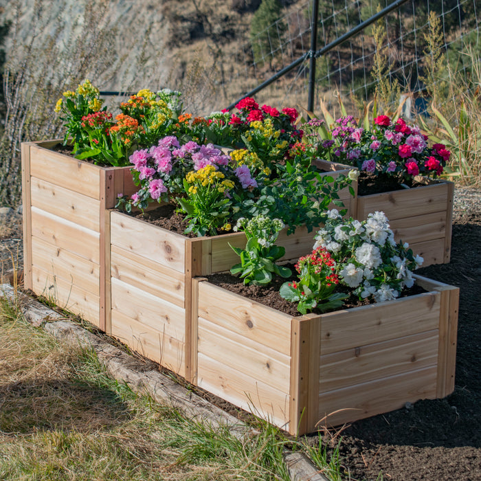 L-Shaped Tiered Raised Garden Bed from Outdoor Living Today planted with pink, yellow, red and white kalanchoe blooms on a hillside plot