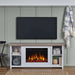 Real Flame Tramore white electric fireplace TV stand styled in a sage green living room with wall-mounted TV above, decorative baskets and books on shelves, jute rug