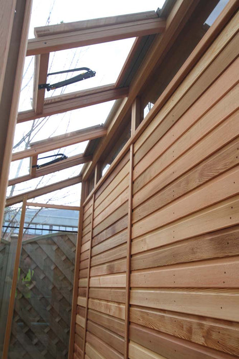 Side view of the Alton Cedar Fusion Greenhouse with open ventilation windows and a wooden panel exterior.