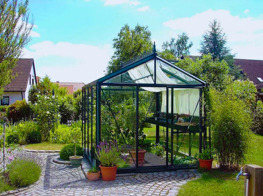  Elegant Exaco Janssens Victorian-style greenhouse VI 23 set in a tranquil garden with a cobblestone path and lush greenery.