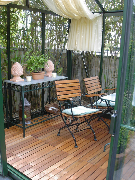 Cozy indoor seating area inside Victorian VI 23 greenhouse, featuring wooden chairs, potted plants, and soft draped curtains for a relaxing garden retreat.