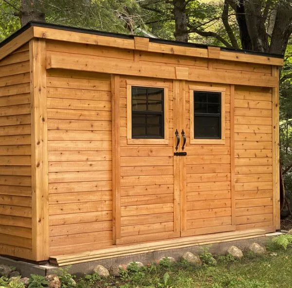 GardenSaver 12x4 cedar storage shed with sliding doors placed in wooded outdoor setting on concrete foundation.