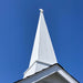 Tall white Little Cottage chapel steeple with a cross at the peak, photographed against a clear blue sky for church and architectural design inspiration