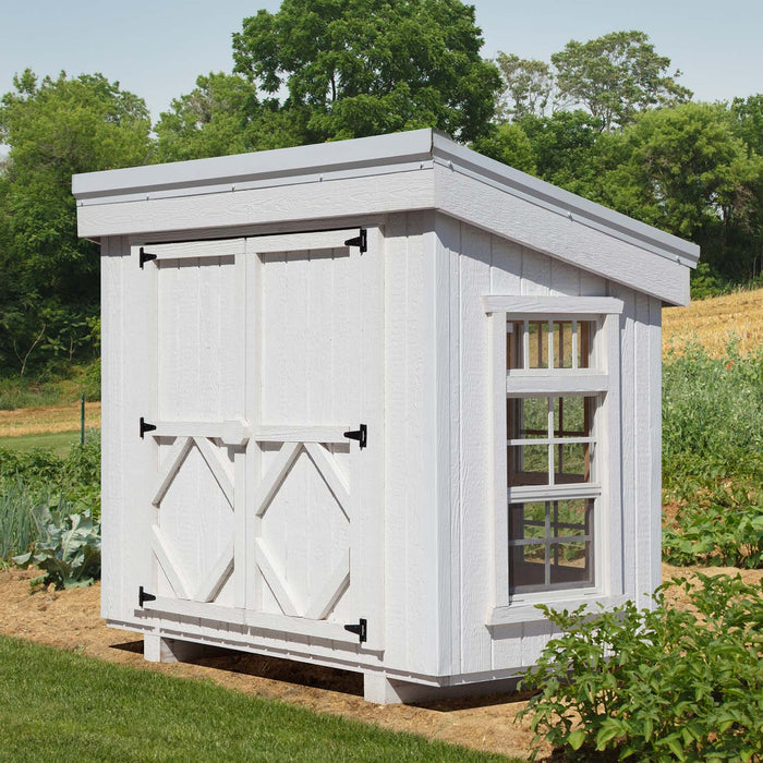 Exterior of Petite Greenhouse from Little Cottage Co., painted white with barn-style doors, side windows, and slanted roof for backyard gardens