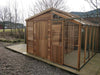 Wide view of the Alton Cedar Fusion Greenhouse with closed doors, showing the side glass panels and wooden frame. 