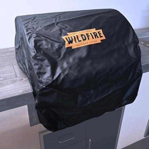 Close-up of the Wildfire Ranch Pro built-in grill covered with a black protective cover showcasing the Wildfire logo