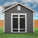 A Handy Home Windemere 10x12 - Wood Storage Shed, in dark gray with white trim, features double doors and a small attic window. Set against a wooden fence under a partly cloudy sky, this weather-resistant structure offers ample storage for all your needs.