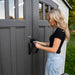 Close-up of a woman locking the Lifetime 8x10 Shed, showcasing the secure door mechanism and elegant exterior.