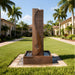 Brown stone Yang outdoor water fountain featuring curved textured design and square basin, styled in a luxury palm-lined courtyard.