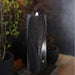 Yang modern tabletop water fountain with vertical textured panel and soft LED glow, styled indoors with plants for cozy ambiance.